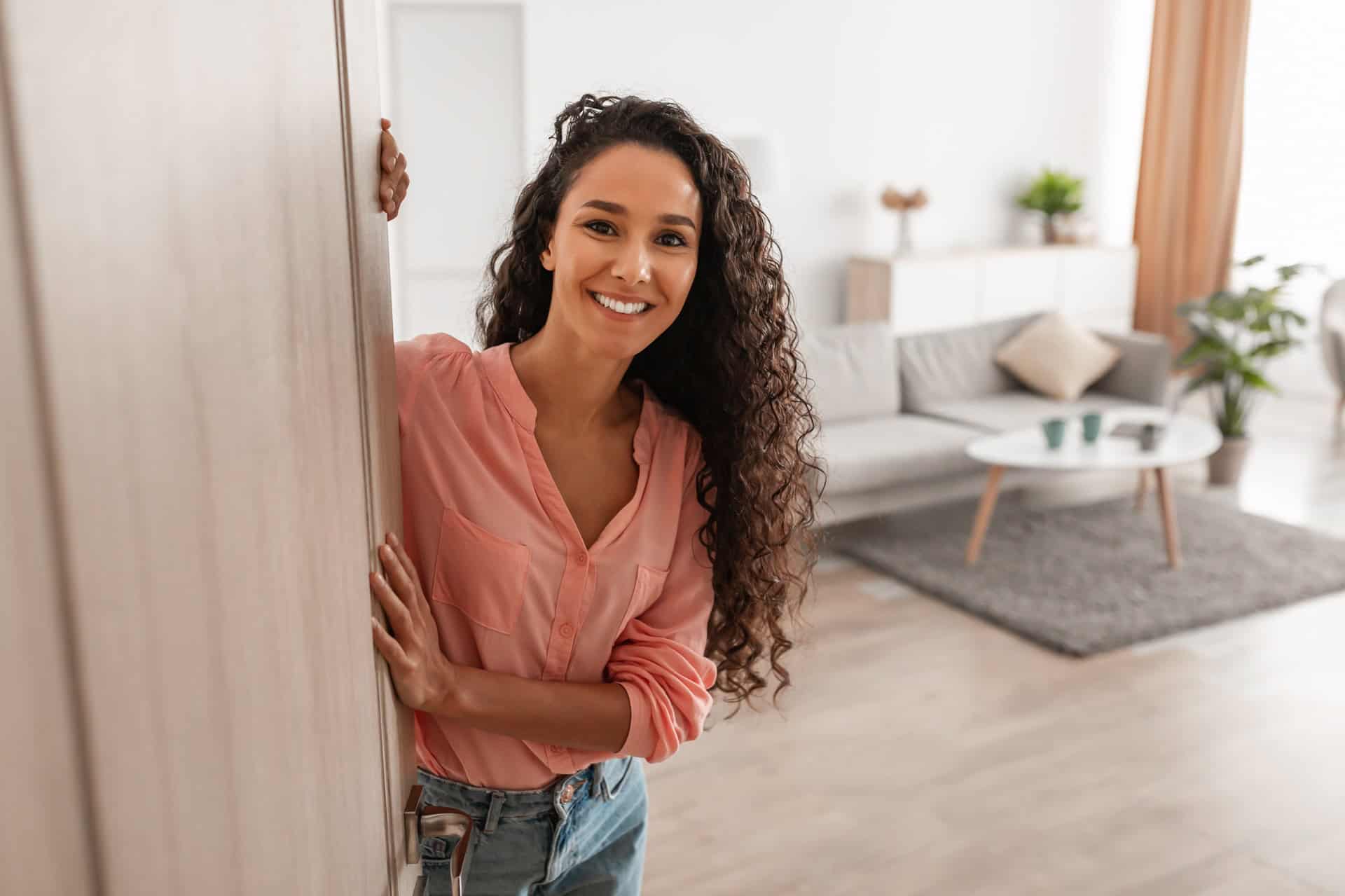 Cheerful young curly lady inviting people to enter home